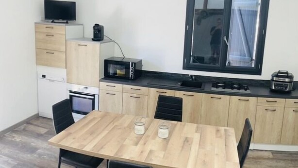 Una cocina compacta con una mesa de madera, sillas negras, un microondas y un refrigerador pequeño.