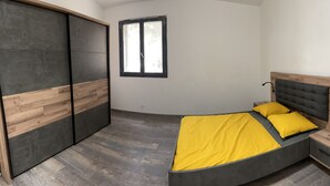 Un dormitorio con cama, mesita de noche, armario y ventana.