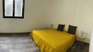 Una habitación con una cama, dos lámparas de noche, una mesita con lámpara y un ventanal con persianas.