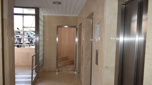 A hallway with a metal elevator, a staircase, and a glass door leading to a parking area.