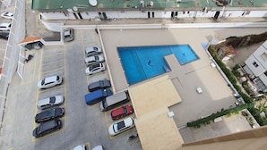An aerial view of a parking lot with a swimming pool, surrounded by buildings.
