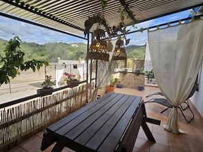 A covered outdoor seating area with a wooden table, potted plants, and a view of a green landscape. - Country House 'Experience Alpacas in Andalucia' with Mountain View (Montoro)