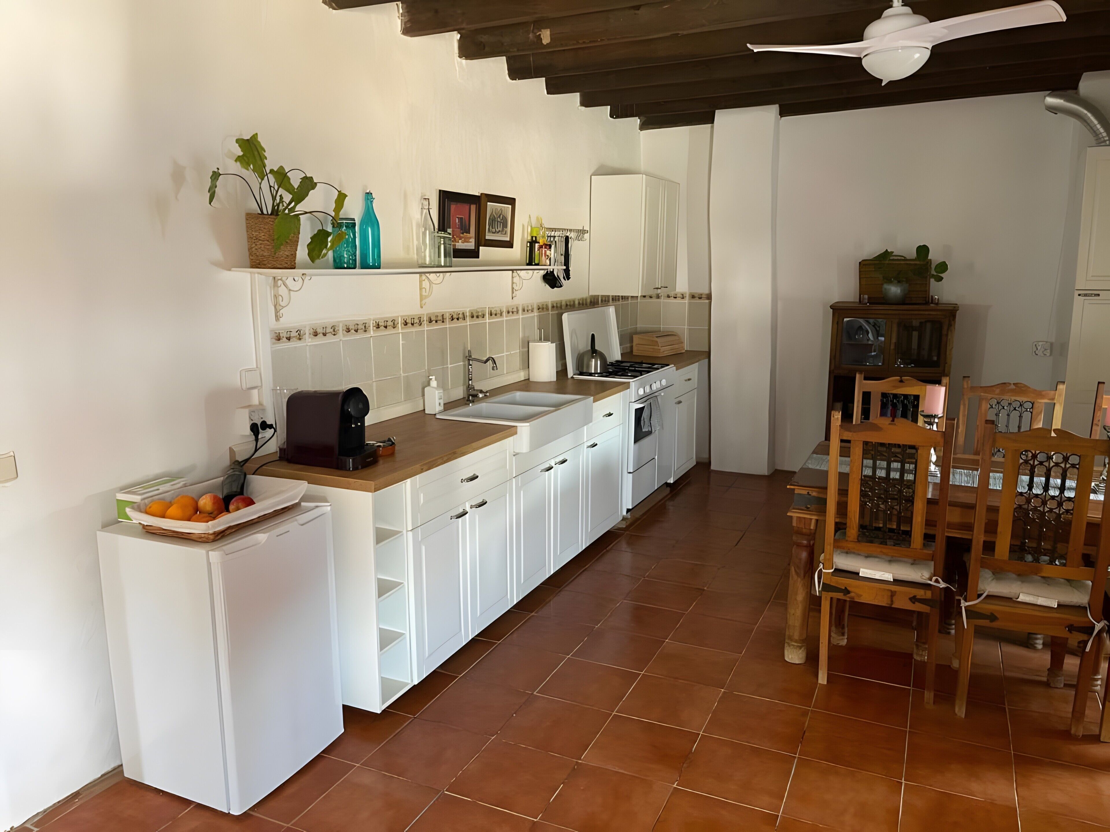 Una cocina con armarios blancos, encimera de madera, fregadero, estufa y zona de comedor con sillas de madera.