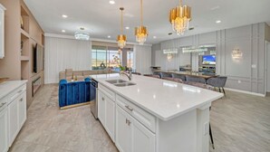 Une cuisine spacieuse dotée d’un grand îlot central, de luminaires suspendus modernes et d’un coin repas avec un bar.
