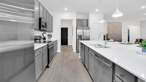 A modern kitchen with stainless steel appliances, a large island with a sink, and a black door leading to another room. - Luxury Contemporary Style Mansion on Veranda Palms Resort Orlando Mansion 5545 (Kissimmee)