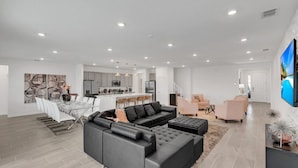 A spacious living area with a sectional sofa, a dining table, and a kitchen in the background. - Imagine Your Family Renting This Luxury Contemporary Style Mansion on Veranda Palms Resort Orlando Mansion 5546 (Kissimmee)