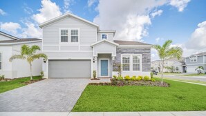 A two-story residential house with a garage, a front yard with grass and small plants, and a clear sky. - Your Beautiful 5 Star Villa Minutes From Disney on the Prestigious Windsor Island Resort, Orlando Villa 5566 (Kissimmee)