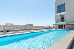 Uma piscina com superfície de água azul cristalina, rodeada por edifícios modernos com varandas e grandes janelas.