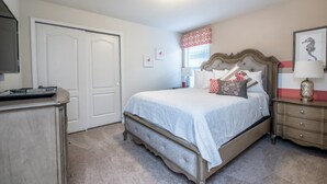 Quarto com cama, cômoda e televisão sobre um suporte.