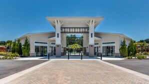 A modern building with a large entrance, paved walkway, and surrounding greenery. - Amazing Villa on Veranda Palms Resort With Private Pool, Orlando Villa 5626 (Kissimmee)