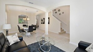 A spacious living area with a modern sofa, a glass coffee table, and a dining area with a chandelier. - Amazing Villa on Veranda Palms Resort With Private Pool, Orlando Villa 5626 (Kissimmee)