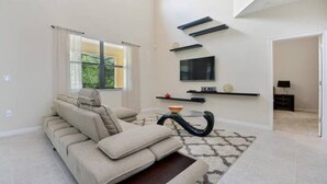 A modern living room with a beige sofa, a glass coffee table, and a TV mounted on the wall. - Amazing Villa on Veranda Palms Resort With Private Pool, Orlando Villa 5626 (Kissimmee)