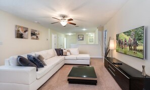 A living room with a white sectional sofa, a black coffee table, a ceiling fan, and a TV on the wall. - Luxury 8 Bedroom Mansion on Champions Gate Resort, Orlando Mansion 5642 (Davenport)