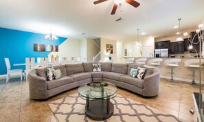 A modern living room with a sectional sofa, a glass coffee table, and a kitchen in the background. - Luxury 8 Bedroom Mansion on Champions Gate Resort, Orlando Mansion 5642 (Davenport)