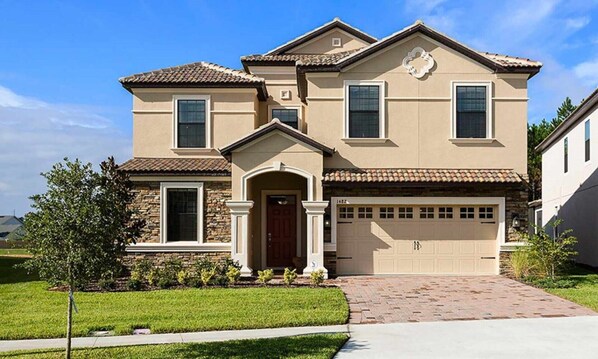 A two-story house with a stone facade, a front entrance with a door, and a garage. - Luxury 8 Bedroom Mansion on Champions Gate Resort, Orlando Mansion 5642 (Davenport)