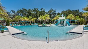 A swimming pool with a slide, surrounded by palm trees and lounge chairs. - Spacious 12 Bedroom Oasis 5649 (Kissimmee)