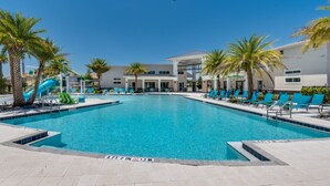 A swimming pool with a water slide, surrounded by palm trees and lounge chairs. - Spacious 12 Bedroom Oasis 5649 (Kissimmee)