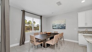 Een moderne keuken met witte kasten, een granieten aanrechtblad en een eethoek met een donker houten tafel en beige stoelen.
