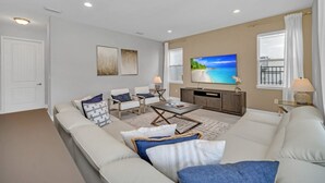 Een woonkamer met een beige bank, twee fauteuils, een salontafel en een flatscreen televisie aan de muur.