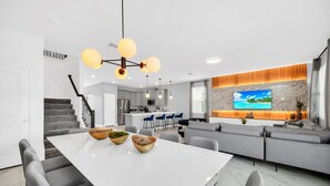Eine moderne Küche mit einer zentralen Kochinsel, einem Essbereich mit weißem Tisch und einem Wohnbereich mit grauem Sofa.