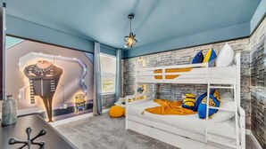 Ein Stockbett, eine Steinsandsteinwand im Hintergrund, ein Schreibtisch mit einer besonderen Lampe und eine Wanddekoration mit Minion-Motiv.
