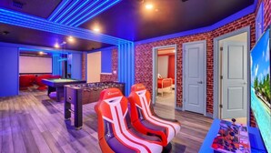 A room with a foosball table, two red and white gaming chairs, a pool table, and a large screen. - Ultimate Luxury Getaway With 10 Bedrooms 5659 (Kissimmee)