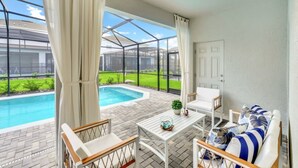 A covered outdoor area with a pool, white furniture, and a view of a green landscape. - Ultimate Luxury Getaway With 10 Bedrooms 5659 (Kissimmee)