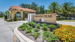 A sign for Veranda Palms with a clear view of the entrance, a small building with a red-tiled roof, and a landscaped area with shrubs and flowers. - Exclusive 5 Star Mansion on Veranda Palms Resort, Orlando Mansion 5670 (Kissimmee)