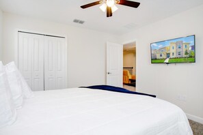 Ein Schlafzimmer mit einem Bett, einem Deckenventilator, einer weißen Tür und einem gerahmten Bild an der Wand.