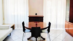 Zona pranzo con un tavolo rotondo, sedie nere, una divanetto bianco e un mobile con ante in vetro.