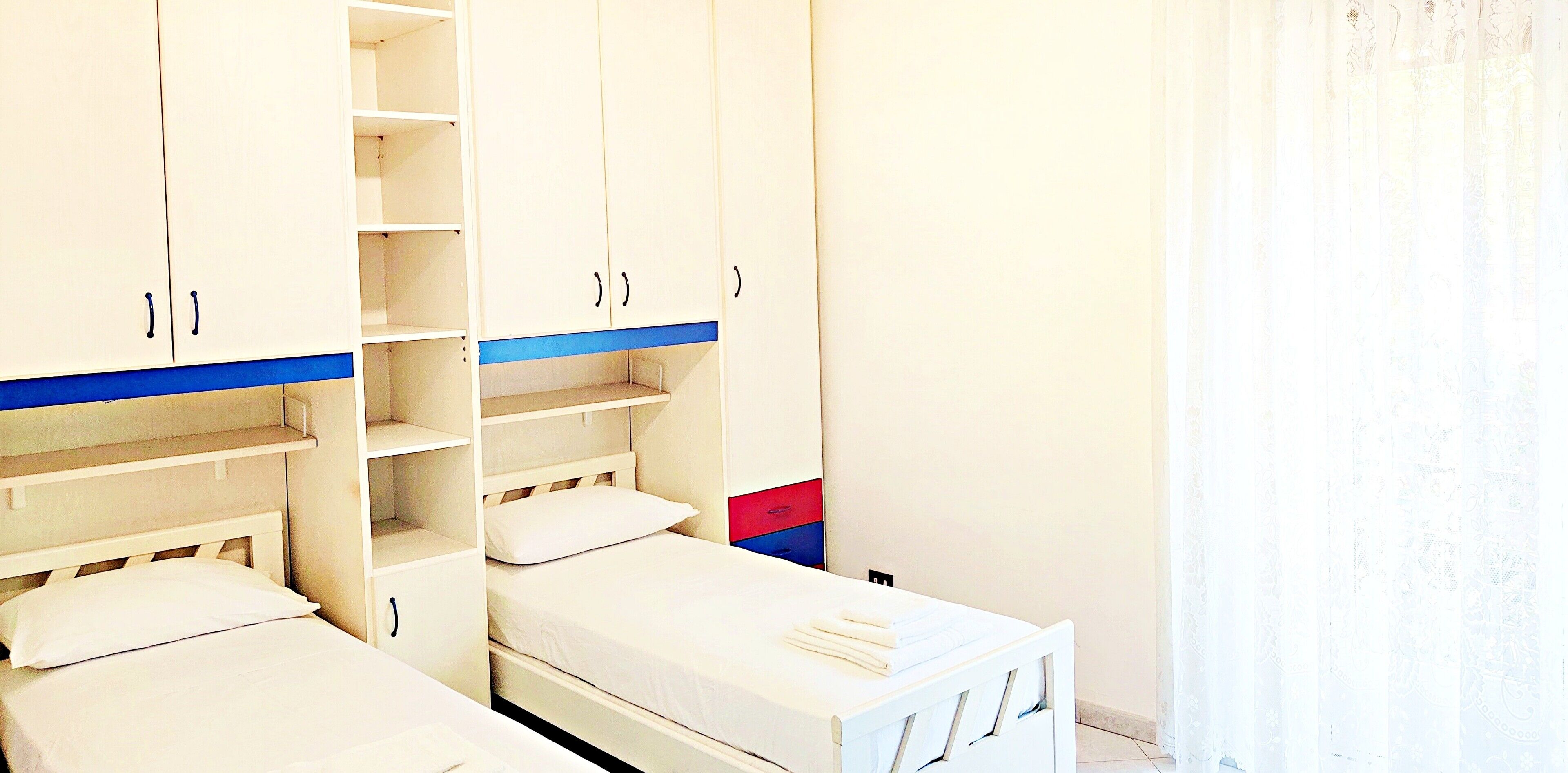 A bedroom with two beds, a wardrobe, and a small table.
