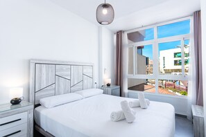 A modern hotel room with a large bed, a bedside table, a lamp, and a view of the city through the window. - Nevada Centro by Casasol (Nerja)