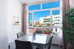 A hotel room with a large window, a table with chairs, a macrame wall hanging, and a potted plant. - Nevada Centro by Casasol (Nerja)