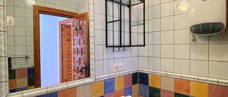 Un baño con pared de azulejos coloridos, un lavabo blanco, un inodoro, un espejo y un secador de pelo en la pared.