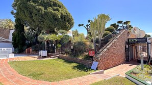 Un jardín ajardinado con un sendero pavimentado, un árbol grande y un edificio con un letrero que dice "KK'S BAR & RESTAURANT".