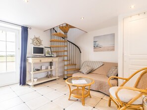 Una sala de estar acogedora con una escalera espiral, un escritorio con computadora, un sofá y un sillón de mimbre.