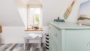 A room with a sloped ceiling, a window with a sailboat model, a small table with a towel, a light blue dresser, and a 'relax' sign.