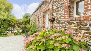 A stone building with a gravel driveway and a garden with pink flowers.