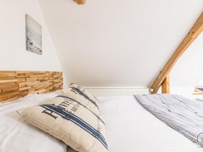 Un dormitorio con techo inclinado, cabecera de madera y cama con dos almohadas.