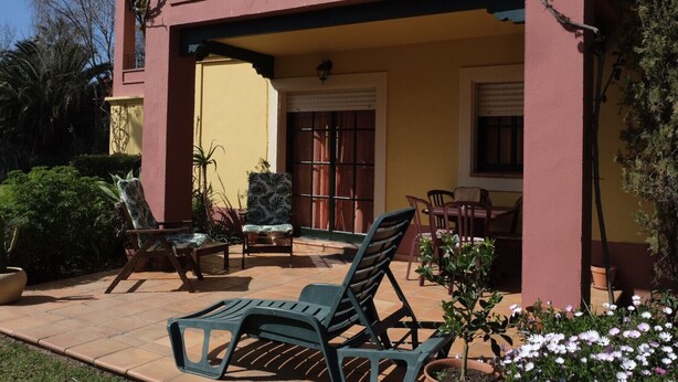 Un patio con mobiliario exterior, una pared amarilla y una columna roja.