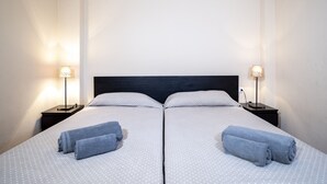 Een tweepersoonsbed met een donkere hoofdbord, twee nachtkastjes met lampen, en twee opgerolde handdoeken op het bed.