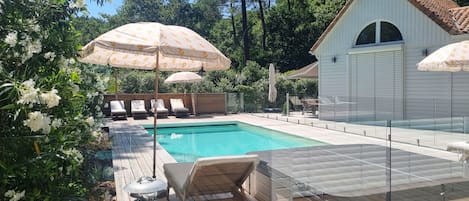 A swimming pool with lounge chairs and umbrellas, surrounded by greenery and a wooden deck.