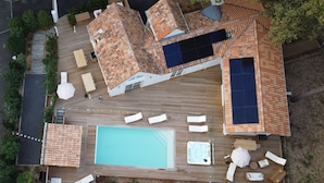 Vista aérea de una terraza en la azotea con piscina, tumbonas, bañera de hidromasaje y un panel solar.