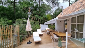 Una terraza de madera con mobiliario exterior, incluyendo una mesa y sillas, y una sombrilla blanca.