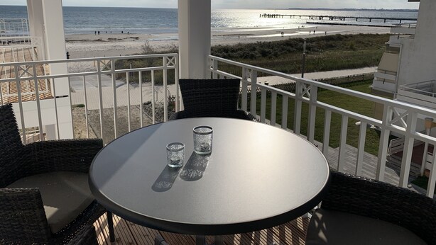 A balcony with a table and chairs, overlooking a beach and a pier. - Sehr Schönes Ferienapartment mit Meerblick an der Ostsee - nur 25 Meter zum Stra (Großenbrode)