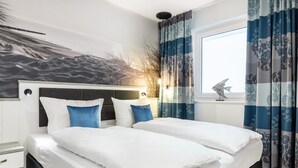 A modern bedroom with a large bed, two pillows, a nightstand, a decorative fish, and a window with curtains. - Sehr Schönes Ferienapartment mit Meerblick an der Ostsee - nur 25 Meter zum Stra (Großenbrode)