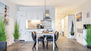 A modern kitchen with white cabinets, a wooden countertop, and a dining area with a table and chairs. - Sehr Schönes Ferienapartment mit Meerblick an der Ostsee - nur 25 Meter zum Stra (Großenbrode)