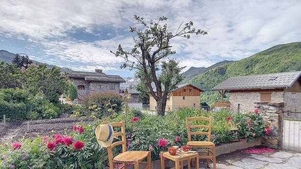 Two wooden chairs in a garden with stone flooring, surrounded by flowering plants and a stone wall. - Family chalet in the center of St Marcel with terrace for 6. (Saint-Martin-de-Belleville)