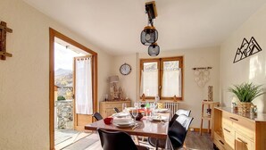 A dining area with a wooden table, black chairs, and a view of the mountains through the windows. - Family chalet in the center of St Marcel with terrace for 6. (Saint-Martin-de-Belleville)