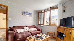 A living room with a brown leather sofa, a wooden coffee table, a TV on a wooden cabinet, and a window with a view of the outdoors. - Family chalet in the center of St Marcel with terrace for 6. (Saint-Martin-de-Belleville)